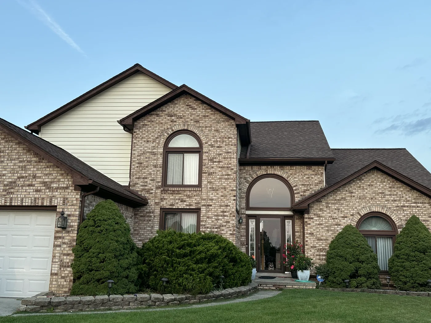 A brick house with arched windows and freshly painted brown trim.