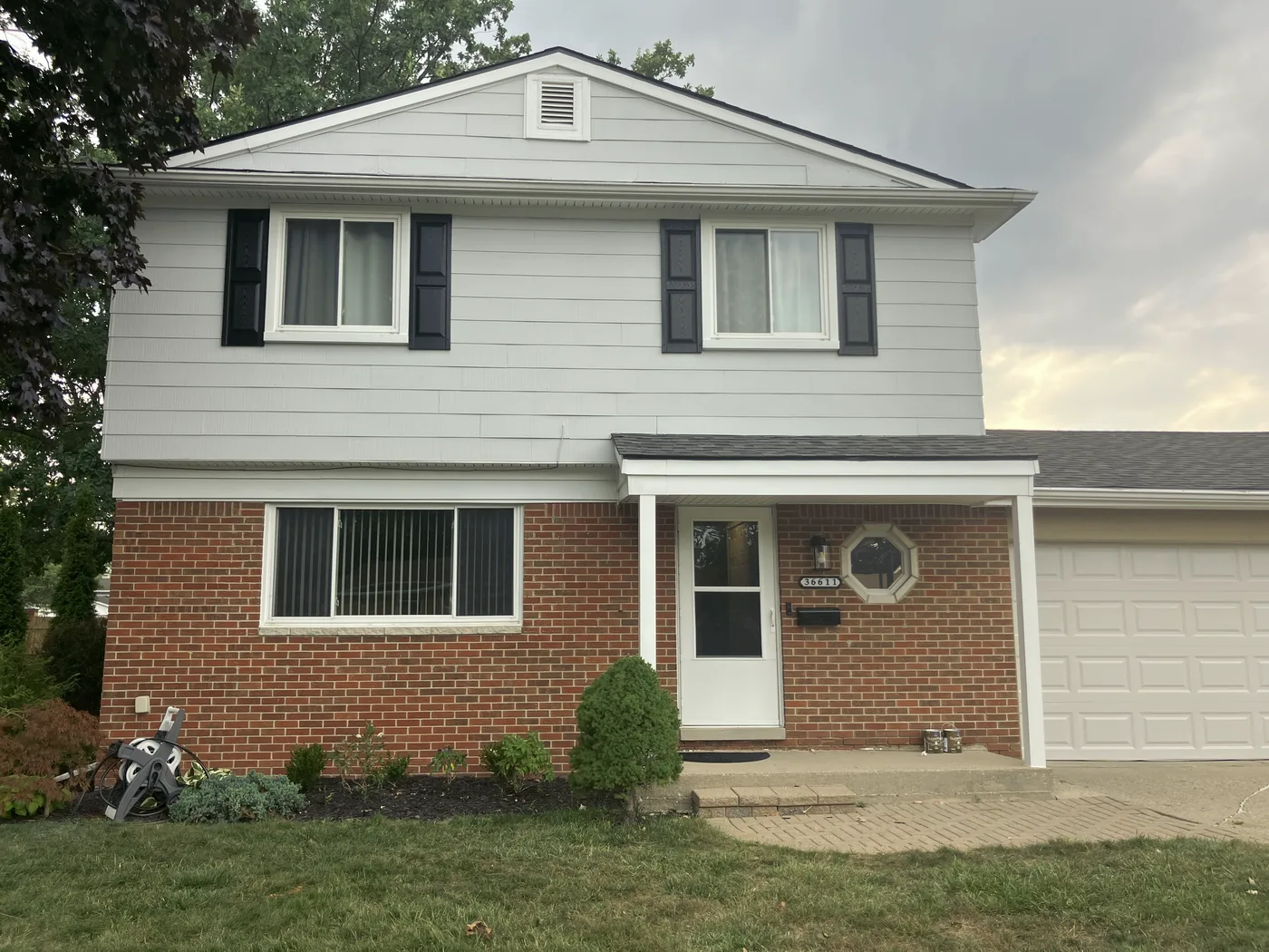 A white colonial with black shutters and a brick base.