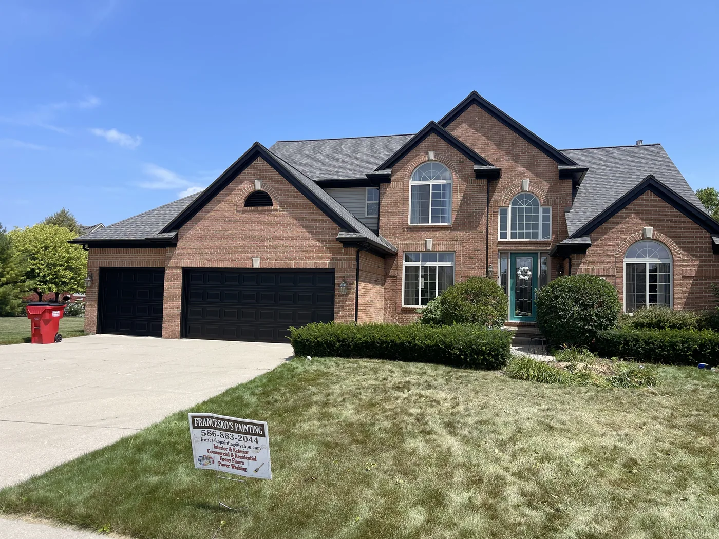 A brick colonial with a black garage door and Francesko's Painting yard sign on the lawn.